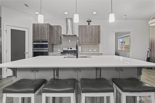 kitchen featuring a kitchen bar, wall chimney range hood, hanging light fixtures, and tasteful backsplash