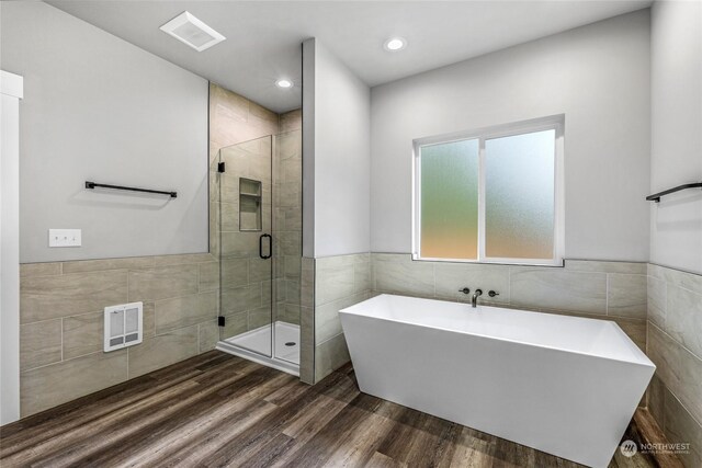 bathroom with plus walk in shower, hardwood / wood-style flooring, and tile walls