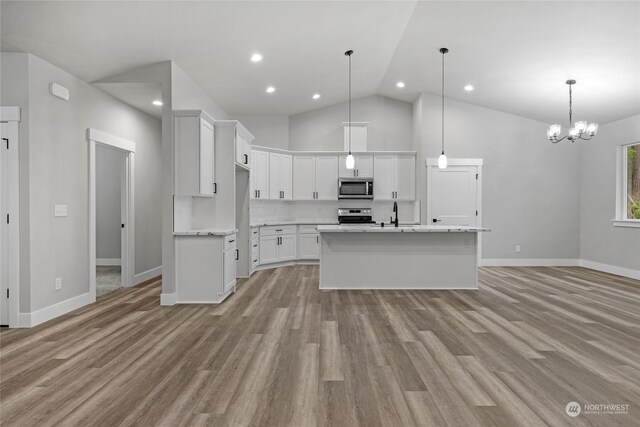 kitchen featuring white cabinetry, hanging light fixtures, stainless steel appliances, high vaulted ceiling, and a kitchen island with sink