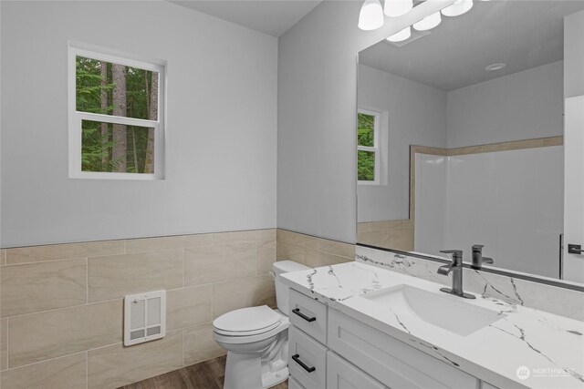 bathroom with walk in shower, vanity, wood-type flooring, tile walls, and toilet