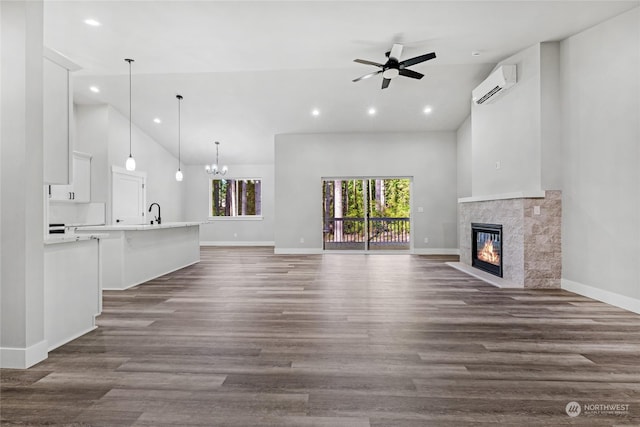 unfurnished living room with dark wood-type flooring, a high ceiling, ceiling fan with notable chandelier, a fireplace, and a wall mounted AC