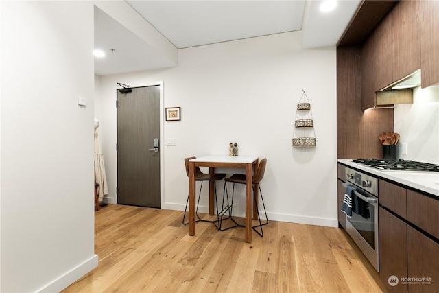 kitchen featuring dark brown cabinetry, decorative backsplash, light hardwood / wood-style flooring, and stainless steel appliances