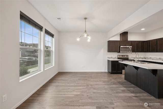 kitchen featuring appliances with stainless steel finishes, hanging light fixtures, a kitchen bar, dark brown cabinetry, and sink