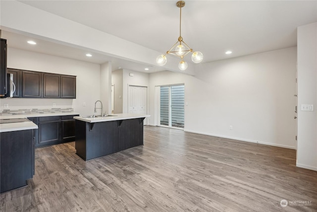 kitchen featuring sink, a kitchen island with sink, wood-type flooring, hanging light fixtures, and a breakfast bar