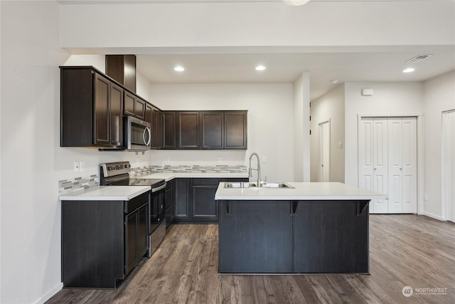 kitchen featuring stainless steel appliances, decorative backsplash, a kitchen island with sink, wood-type flooring, and sink