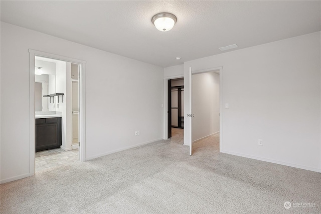 unfurnished bedroom with ensuite bath, a textured ceiling, and light carpet