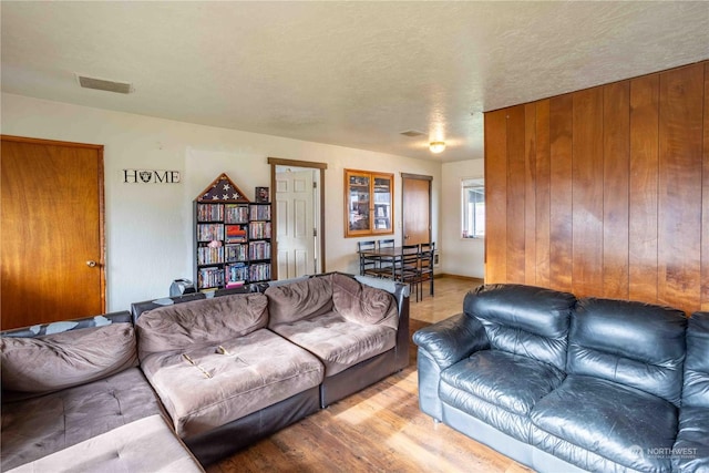 living room with light wood-type flooring, a textured ceiling, and wood walls