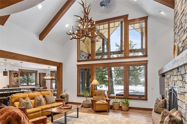 living room featuring beam ceiling, high vaulted ceiling, a notable chandelier, light hardwood / wood-style floors, and a fireplace