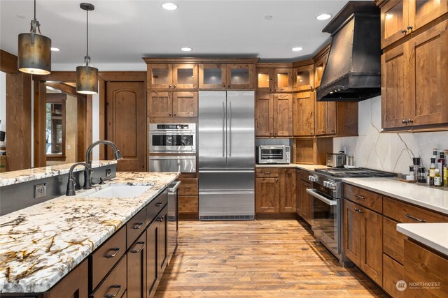 kitchen with sink, light hardwood / wood-style flooring, pendant lighting, custom range hood, and high end appliances