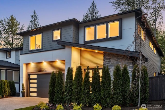 contemporary home with a garage, fence, stone siding, stucco siding, and driveway