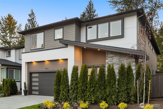 contemporary house featuring concrete driveway, stucco siding, stone siding, and a garage