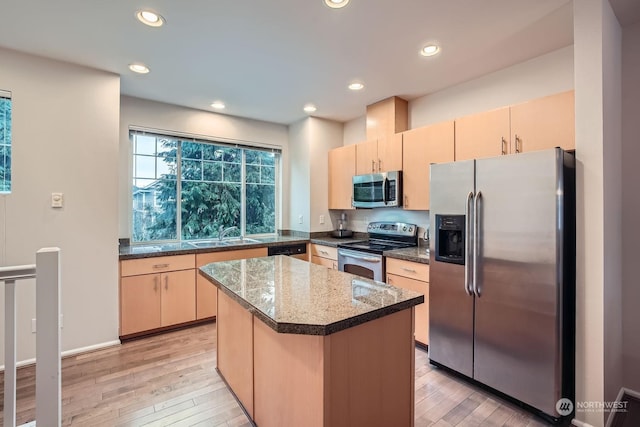 kitchen featuring appliances with stainless steel finishes, sink, dark stone countertops, a center island, and light hardwood / wood-style flooring