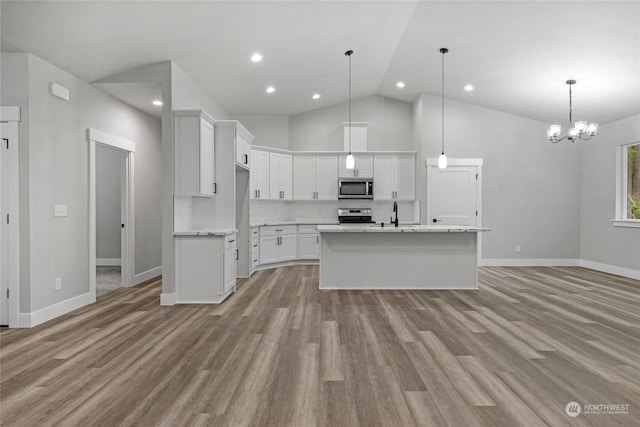 kitchen featuring appliances with stainless steel finishes, high vaulted ceiling, white cabinets, hanging light fixtures, and an island with sink