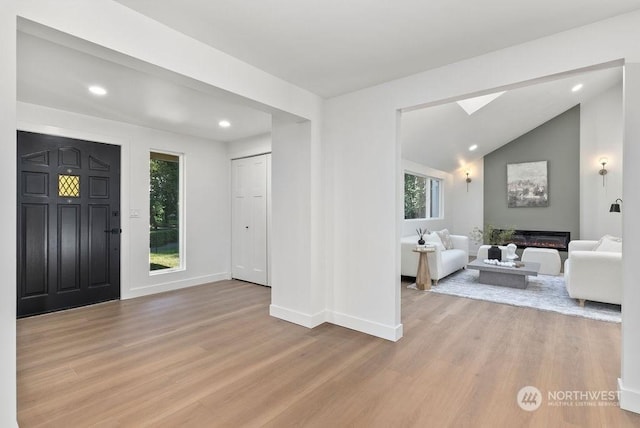 foyer entrance with lofted ceiling with skylight and light wood-type flooring