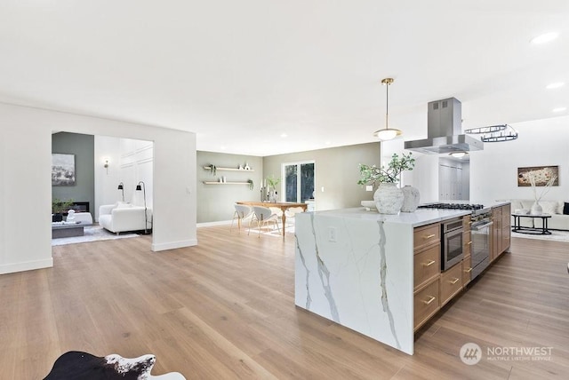 kitchen with light stone countertops, hanging light fixtures, range hood, oven, and light wood-type flooring