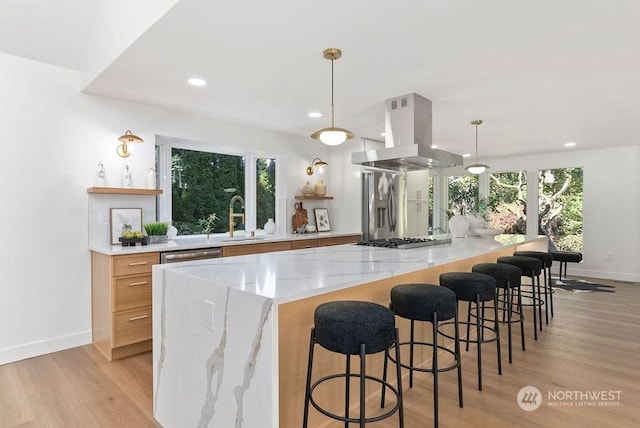 kitchen featuring island exhaust hood, a kitchen breakfast bar, light stone counters, sink, and hanging light fixtures