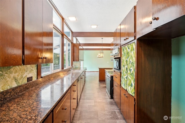 kitchen with a textured ceiling, dark stone counters, sink, hanging light fixtures, and a notable chandelier