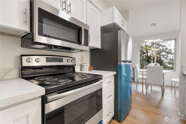 kitchen featuring light stone countertops, appliances with stainless steel finishes, pendant lighting, white cabinets, and light hardwood / wood-style floors