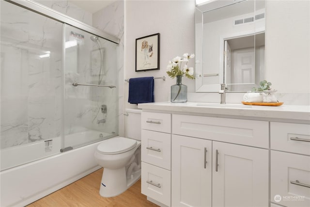 full bathroom with shower / bath combination with glass door, wood-type flooring, vanity, and toilet