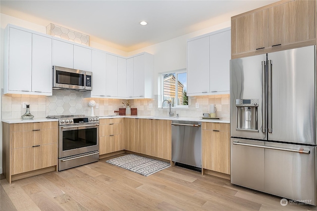 kitchen with sink, light hardwood / wood-style flooring, appliances with stainless steel finishes, tasteful backsplash, and white cabinetry