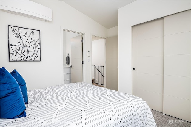 carpeted bedroom featuring vaulted ceiling, connected bathroom, a closet, and a wall mounted air conditioner