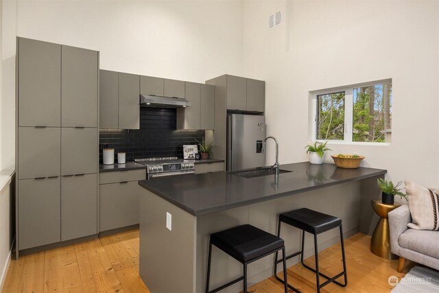 kitchen featuring gray cabinetry, a breakfast bar, sink, decorative backsplash, and stainless steel appliances