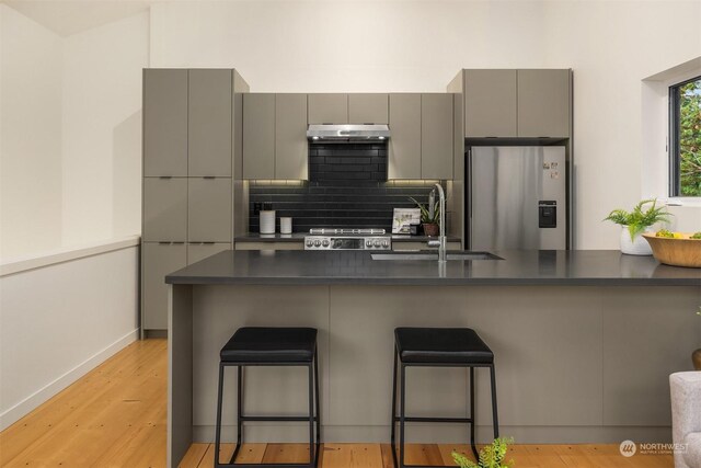 kitchen featuring gray cabinetry, sink, stainless steel fridge with ice dispenser, kitchen peninsula, and a breakfast bar area