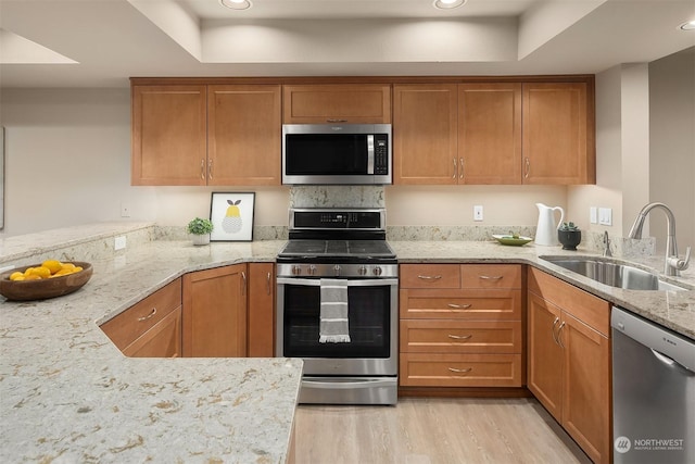 kitchen featuring sink, light hardwood / wood-style flooring, light stone countertops, kitchen peninsula, and stainless steel appliances