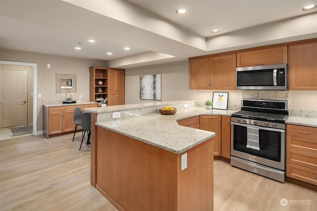 kitchen with light stone countertops, kitchen peninsula, appliances with stainless steel finishes, and light hardwood / wood-style flooring