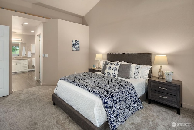 bedroom featuring vaulted ceiling, light colored carpet, sink, and ensuite bath