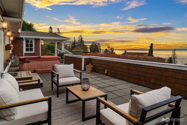 patio terrace at dusk featuring an outdoor living space, a water view, and a hot tub