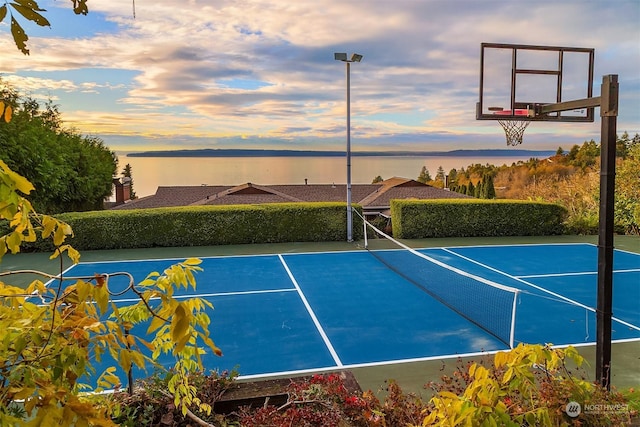 view of sport court with basketball hoop and a water view