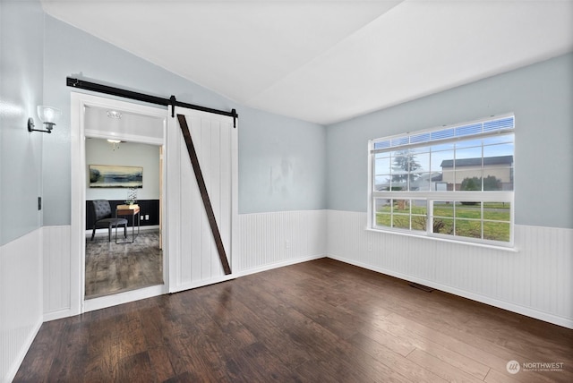 spare room featuring dark hardwood / wood-style floors, a barn door, and lofted ceiling