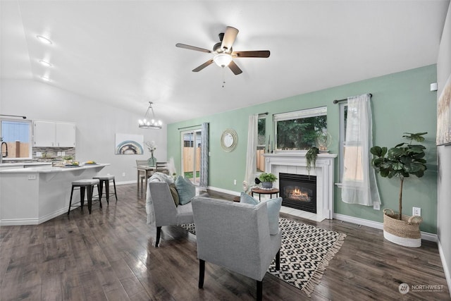 living room featuring ceiling fan with notable chandelier, a tiled fireplace, vaulted ceiling, and dark hardwood / wood-style flooring