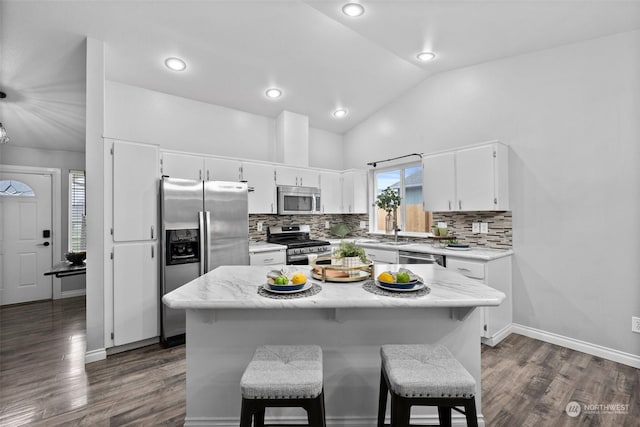 kitchen featuring stainless steel appliances, white cabinets, a center island, vaulted ceiling, and a breakfast bar