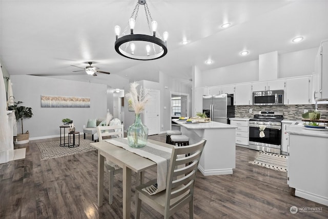 dining room featuring ceiling fan with notable chandelier, vaulted ceiling, and dark wood-type flooring