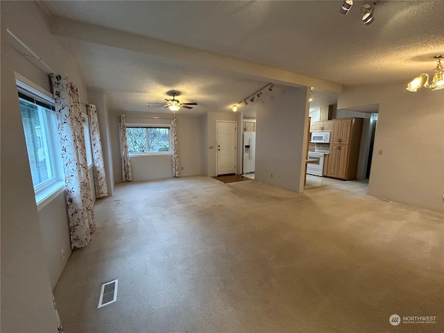 unfurnished living room featuring ceiling fan with notable chandelier, light colored carpet, a textured ceiling, and track lighting