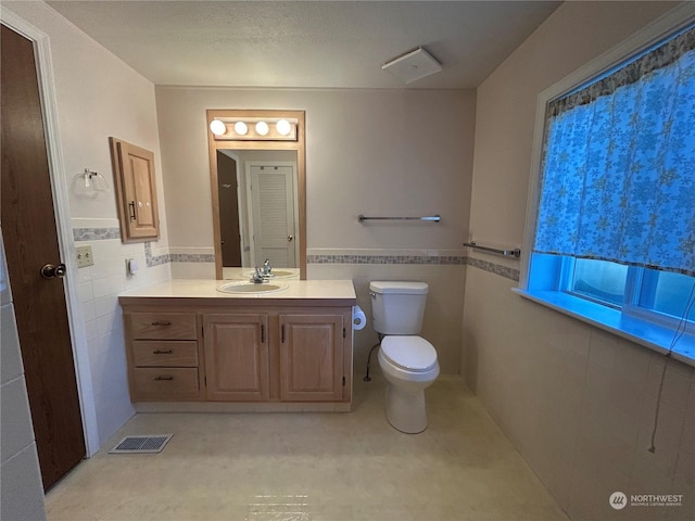 bathroom featuring vanity, toilet, and tile walls