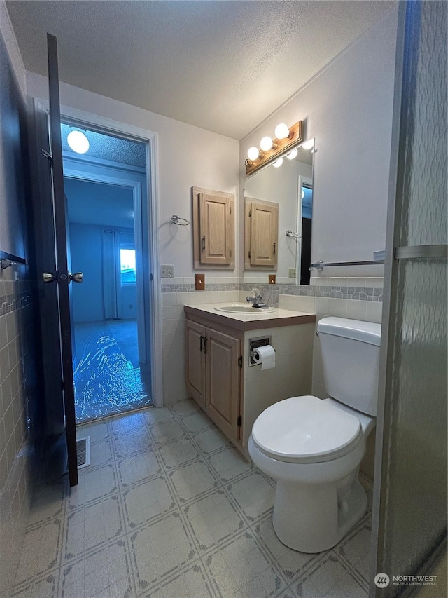 bathroom with a textured ceiling, vanity, tile walls, and toilet