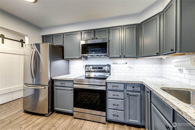 kitchen with decorative backsplash, light stone countertops, gray cabinetry, stainless steel appliances, and light hardwood / wood-style floors