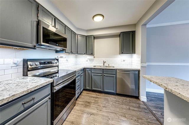 kitchen featuring backsplash, sink, light hardwood / wood-style flooring, gray cabinets, and appliances with stainless steel finishes