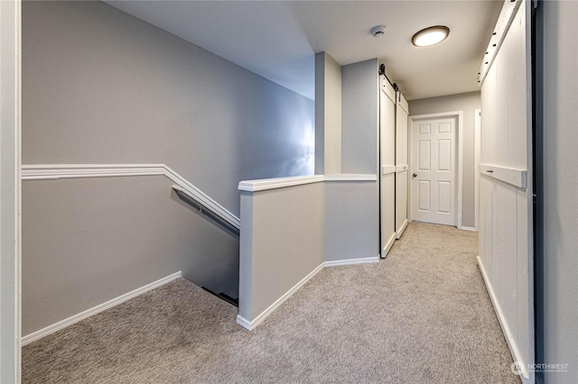 hall featuring a barn door and light colored carpet