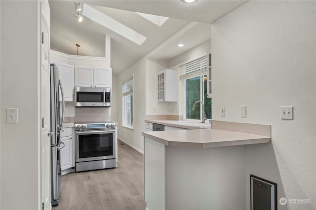 kitchen with lofted ceiling with skylight, white cabinets, sink, appliances with stainless steel finishes, and kitchen peninsula