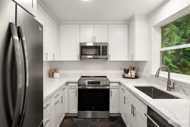 kitchen featuring light stone countertops, stainless steel appliances, white cabinetry, and sink