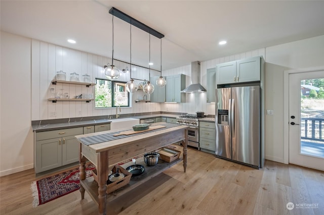 kitchen with sink, hanging light fixtures, wall chimney range hood, light hardwood / wood-style flooring, and appliances with stainless steel finishes