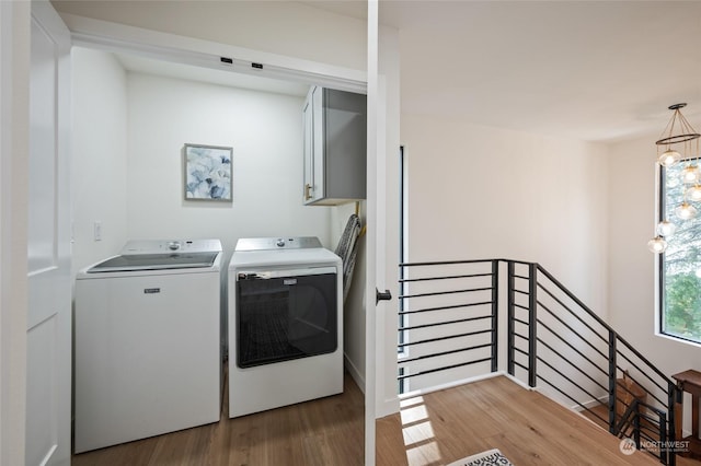 washroom with washing machine and clothes dryer, hardwood / wood-style flooring, cabinets, and a notable chandelier