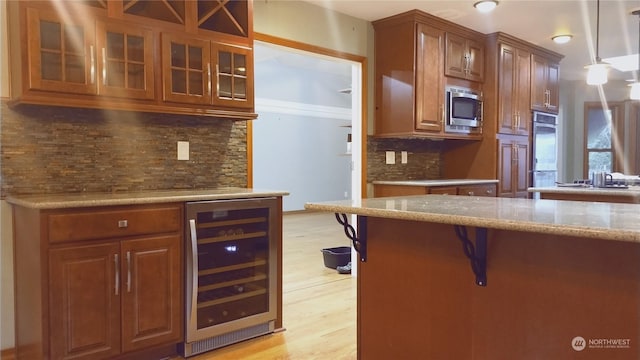 kitchen featuring tasteful backsplash, hanging light fixtures, light wood-type flooring, appliances with stainless steel finishes, and beverage cooler