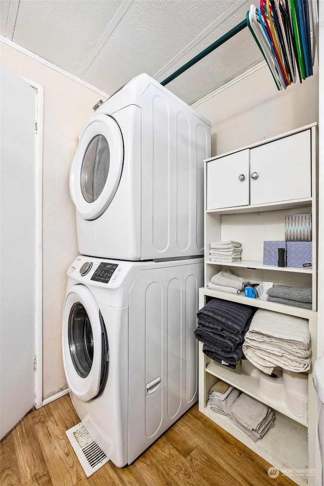 clothes washing area with cabinets, a textured ceiling, stacked washer and dryer, and light hardwood / wood-style flooring