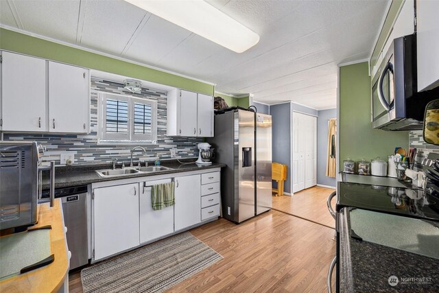 kitchen featuring sink, backsplash, light hardwood / wood-style floors, white cabinets, and appliances with stainless steel finishes