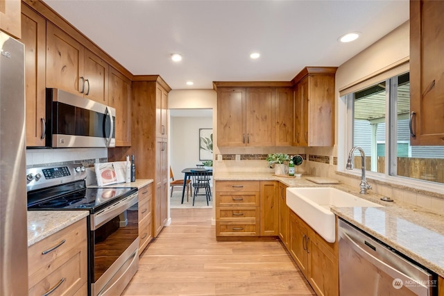 kitchen with light stone countertops, light wood-type flooring, appliances with stainless steel finishes, and sink